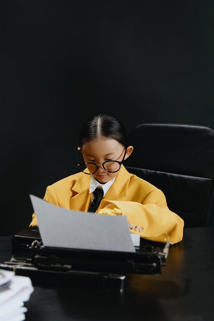 Asian girl in yellow suit reads paper at desk with black background, embodying business creativity.